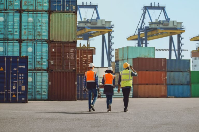 Workers walking through a shipping cargo container terminal depot.