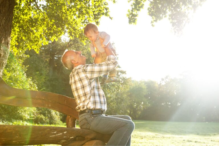 A grandfather playing with his young grandson in a park.